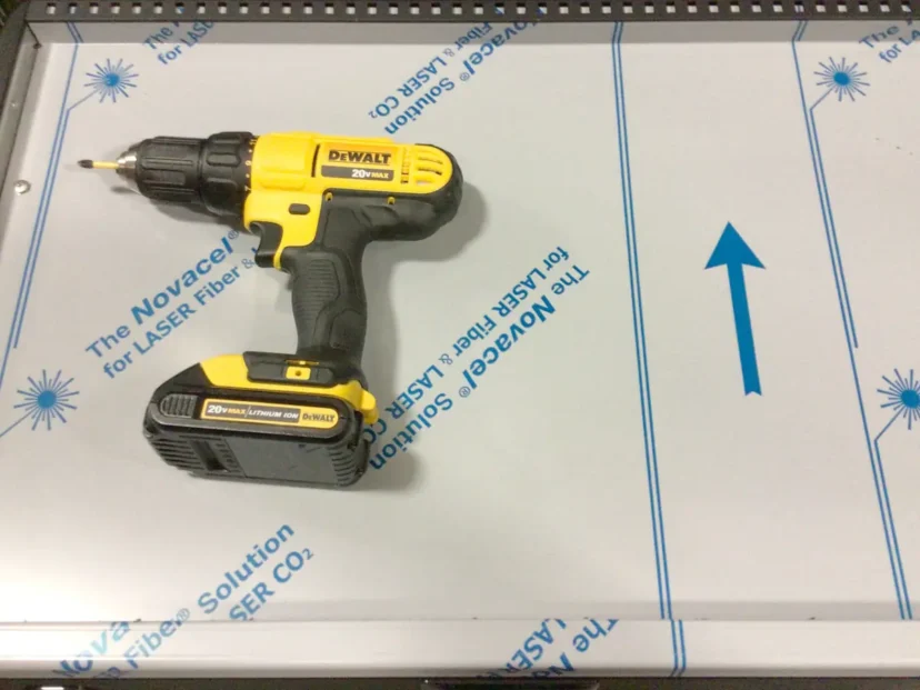 A yellow and black DeWalt cordless drill sits on a sheet labeled The NovaCell for LASER fiber, featuring blue text and a blue arrow pointing right—ideal for precise tasks like Swap Triac installations. © 2025 1st-line.com