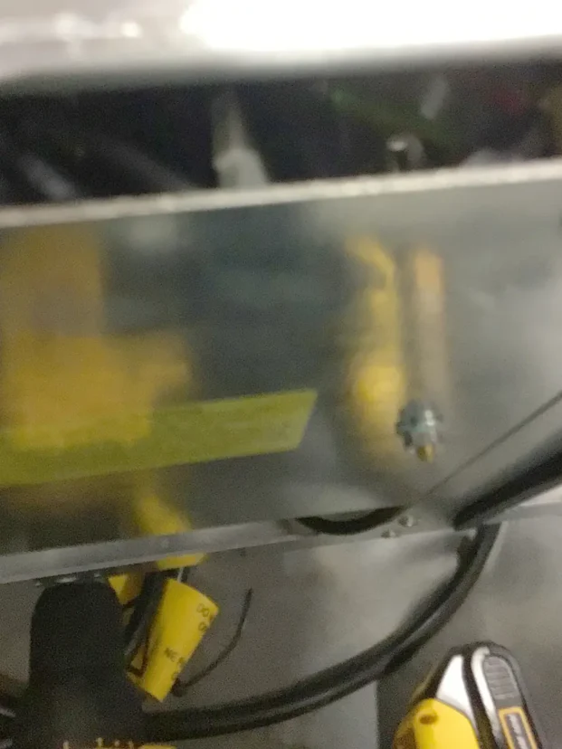 Blurry close-up of a metallic surface with a small screw, yellow labels, and black and yellow wires partially visible at the bottom—possibly part of a Carimali Bubble machine or showing a Swap Triac component. © 2025 1st-line.com
