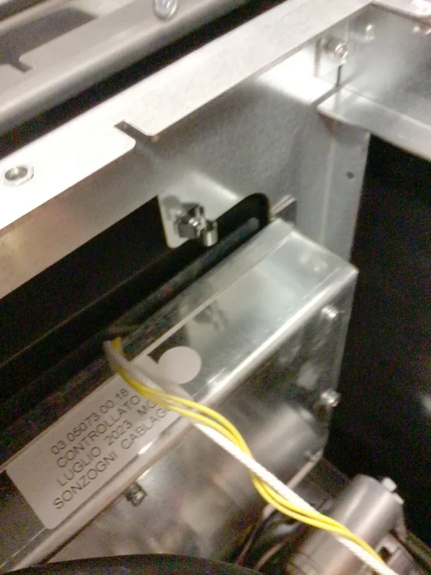 Close-up of a metallic mechanical component with a label, wires attached, and visible screws and brackets inside an electronic or industrial device. © 2025 1st-line.com