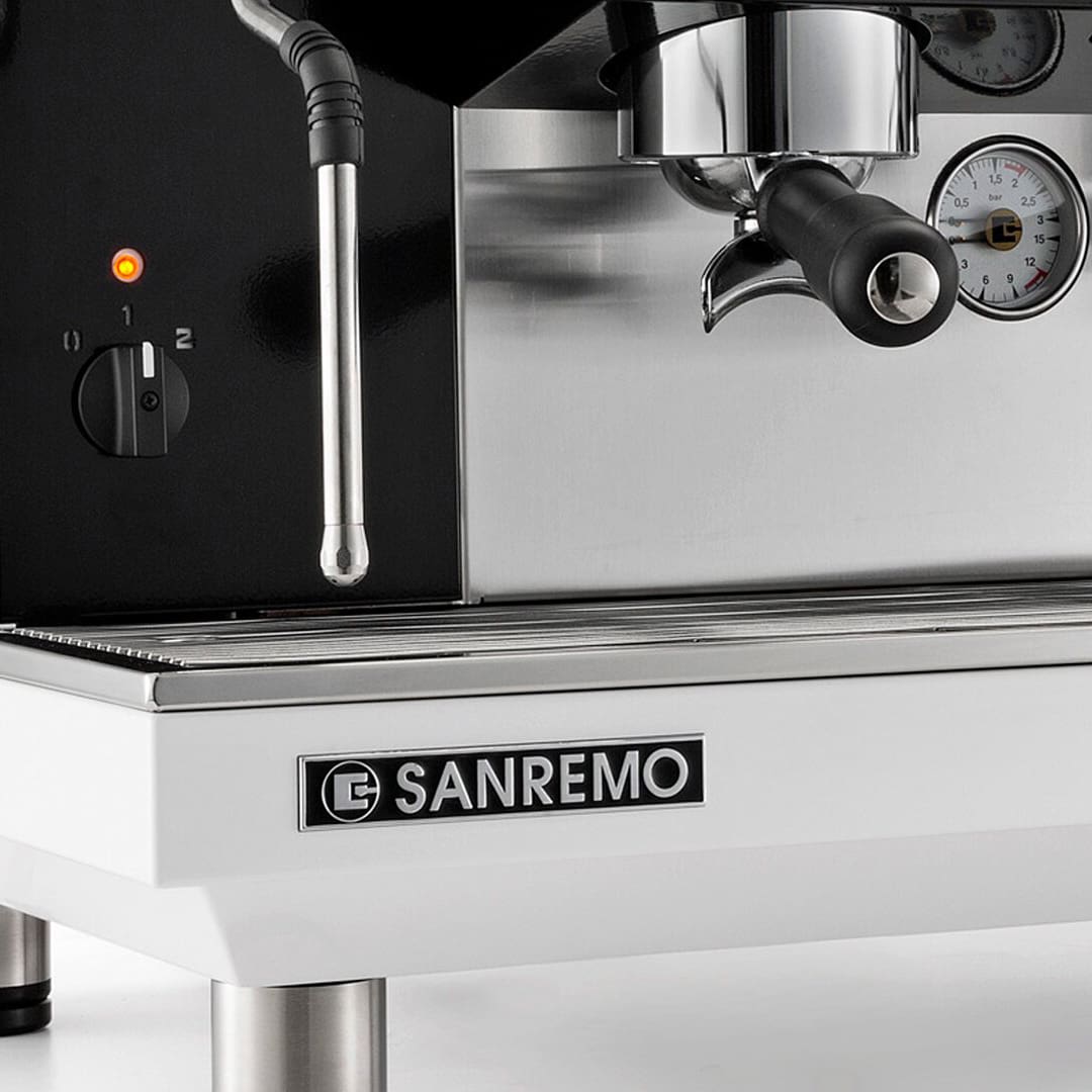 Close-up of a Sanremo espresso machine showing a steam wand, pressure gauges, a portafilter, a control knob with an indicator light, and the Sanremo logo on the front panel. © 2025 1st-line.com