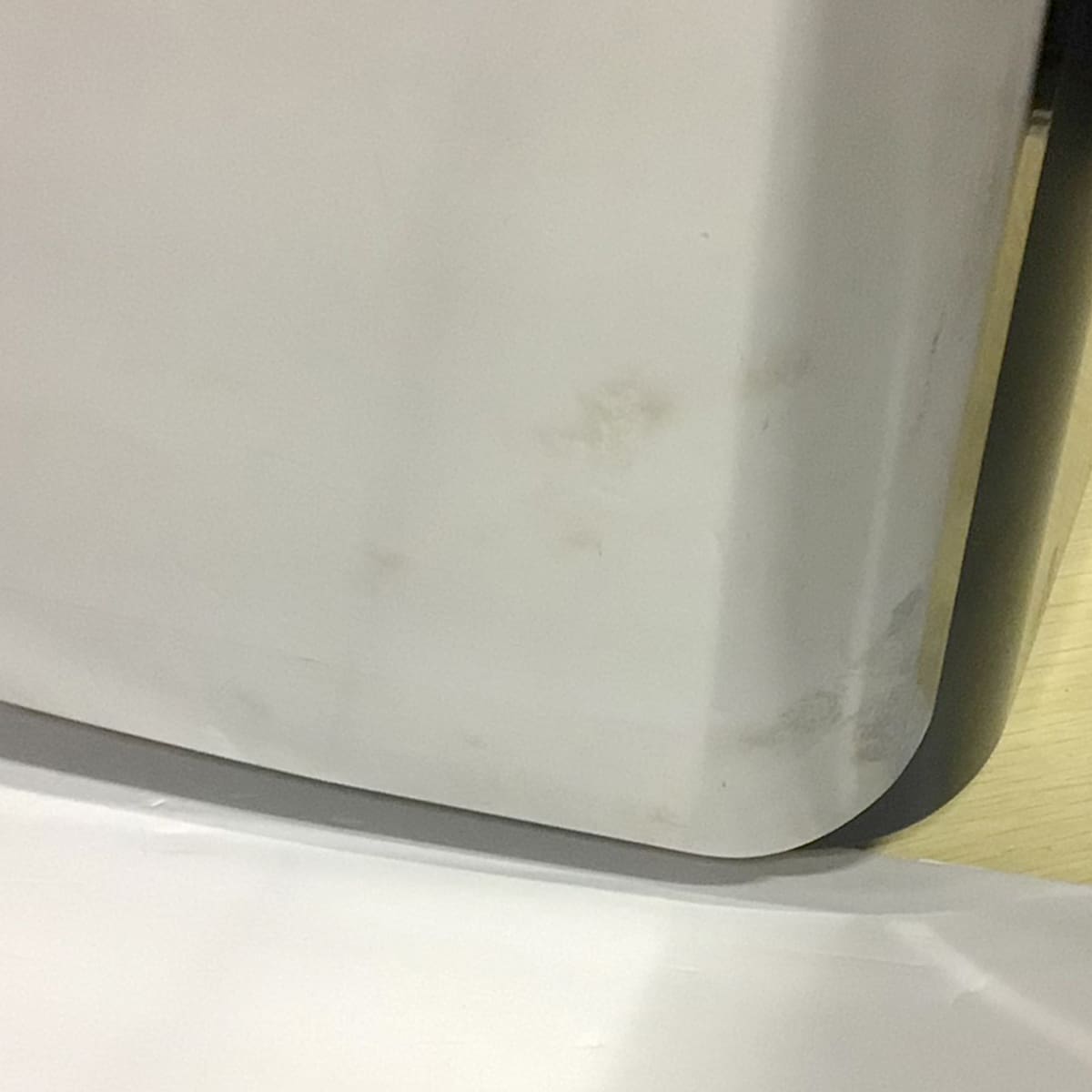 Close-up of a white surface with visible smudges and stains near the edge, bordered by a black frame on the right side and a light-colored wooden floor partially visible in the background. © 2025 1st-line.com