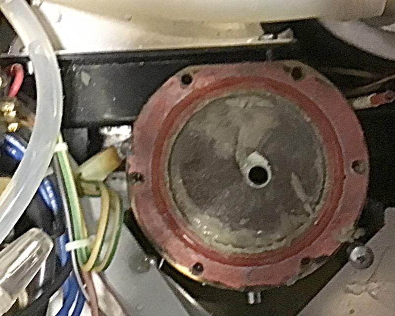 Close-up view of a mechanical component, possibly the Rancilio Silvia Pro X coffee boiler, featuring a central circular metal plate, a red gasket, and various connected wires and tubes—areas where limescale buildup may occur. © 2025 1st-line.com