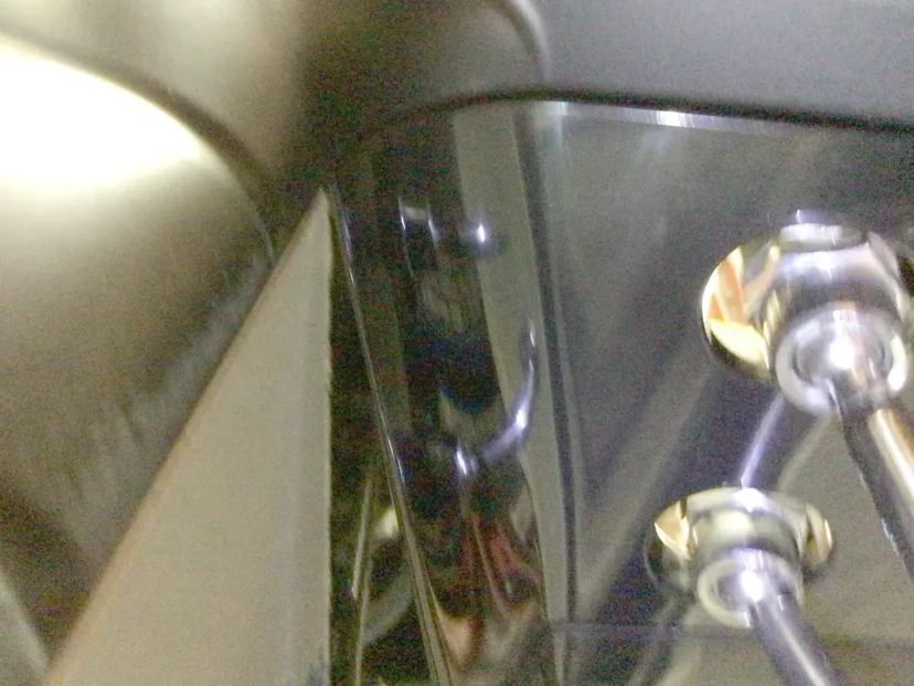 Close-up view of shiny metallic machinery parts, including a reflective black panel and two connected rods with bolts, possibly from Carimali Bubble equipment or featuring a Swap Triac component. © 2025 1st-line.com