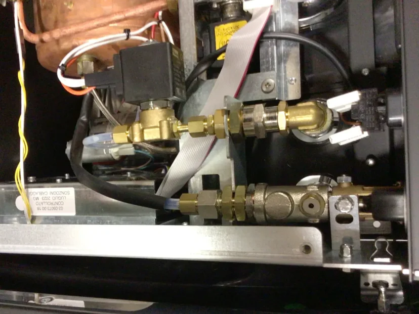 Close-up view of the internal mechanical components and wiring of a Carimali Bubble coffee machine, showing brass valves, metal pipes, connectors, and electronic cables next to the Swap Triac. © 2025 1st-line.com