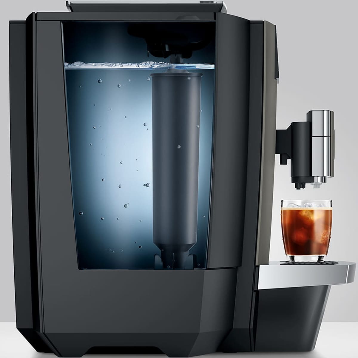 The Jura X10 Super-Automatic Espresso Machine with a transparent water tank is brewing iced coffee into a glass filled with ice on the drip tray. © 2025 1st-line.com