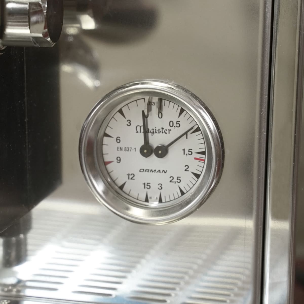 A close-up of a pressure gauge on a stainless steel espresso machine, showing a reading between 1 and 1.5 bar. The dial is labeled Magister and ORMAN. © 2025 1st-line.com