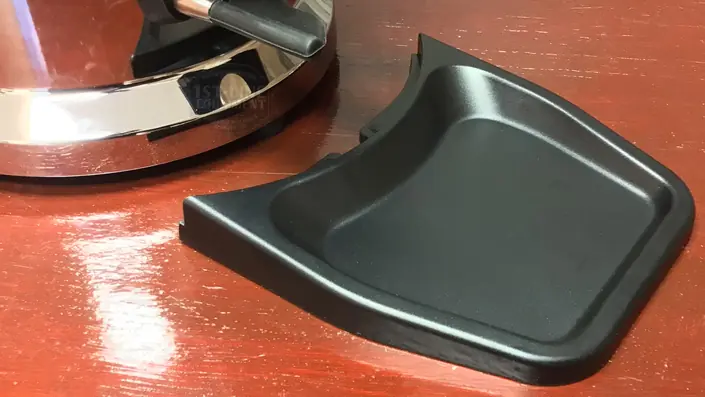 A shiny metallic electric kettle sits on a wooden surface next to a detached black plastic drip tray. © 2025 1st-line.com