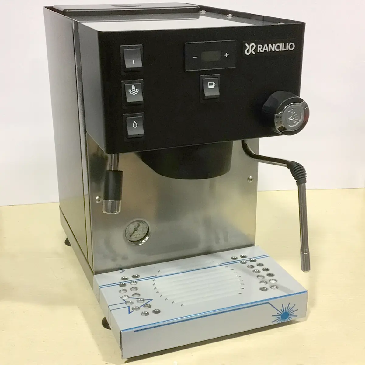 A stainless steel Rancilio espresso machine with black controls, a steam wand, pressure gauge, and buttons for power, brewing, and steam set against a plain background. © 2025 1st-line.com