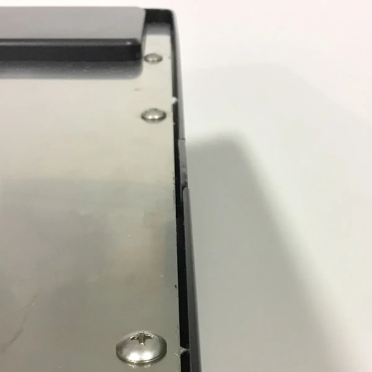 Close-up of the corner of a metal and plastic device, showing several screws on a flat metallic surface and a small gap between the metallic and plastic parts. © 2025 1st-line.com