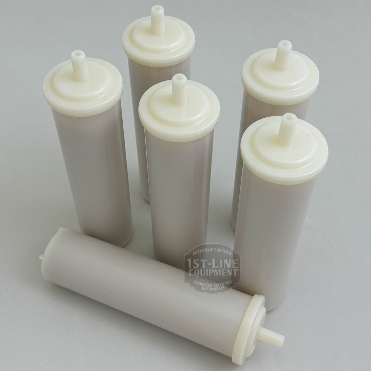 Six 1st-line In-Tank Water Softener / Particle Filter (60 liter) cartridges, featuring white caps, are grouped on a light surface—five upright and one lying down—for use as in-tank softeners or particle filters. © 2025 1st-line.com