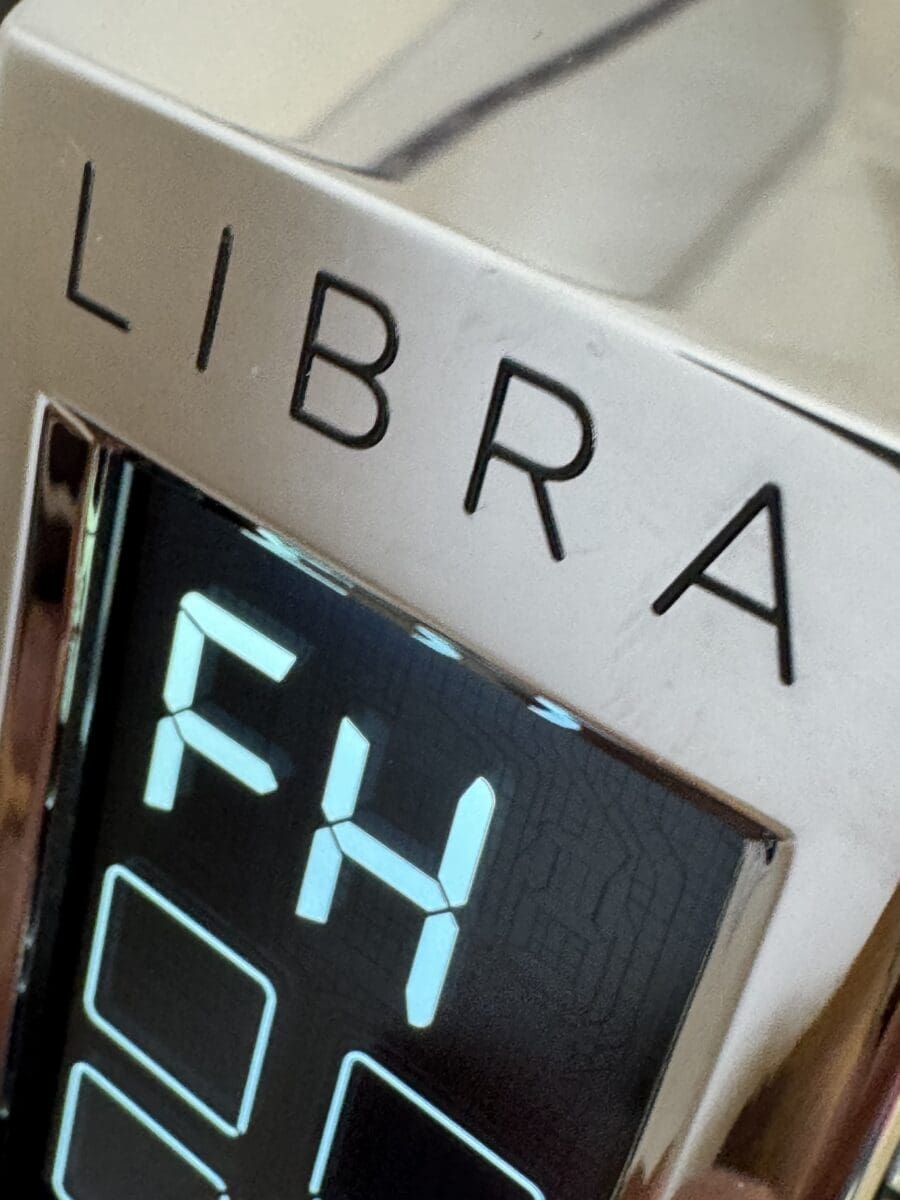 Close-up of a digital display on a shiny metallic Espresso Grinder labeled Eureka Libra. The screen shows the letters “FH” in blue light above several unlit rectangular indicators, suggesting an FH Screen Error. © 2025 1st-line.com
