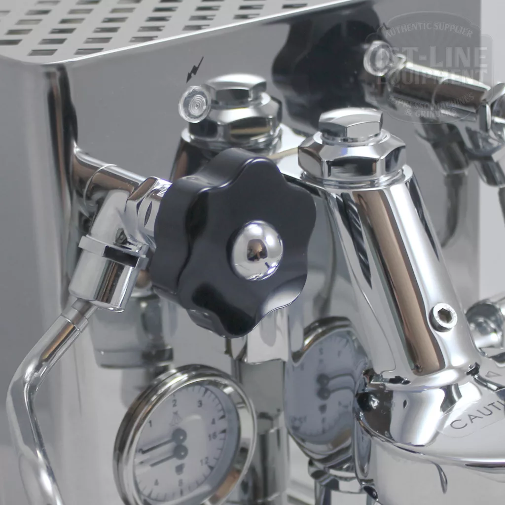 Close-up of a shiny stainless steel espresso machine, showing a black adjustment knob, pressure gauges, and various metal components, reflecting light and surroundings. © 2025 1st-line.com