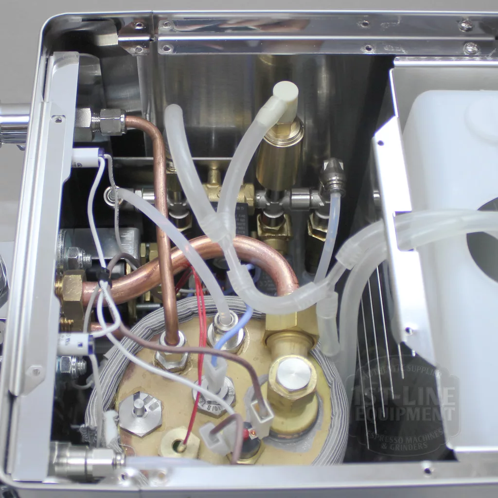 Close-up view of the internal components of an espresso machine, showing copper pipes, plastic tubing, metal parts, and wiring, revealing the machine’s complex plumbing and electrical connections. © 2025 1st-line.com