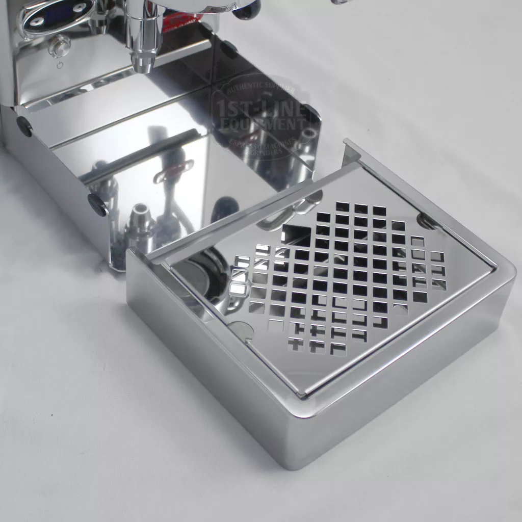 A shiny metal espresso machine drip tray with a grid pattern, partially pulled out on a white surface. The tray reflects light, showing its polished, mirror-like finish. © 2025 1st-line.com