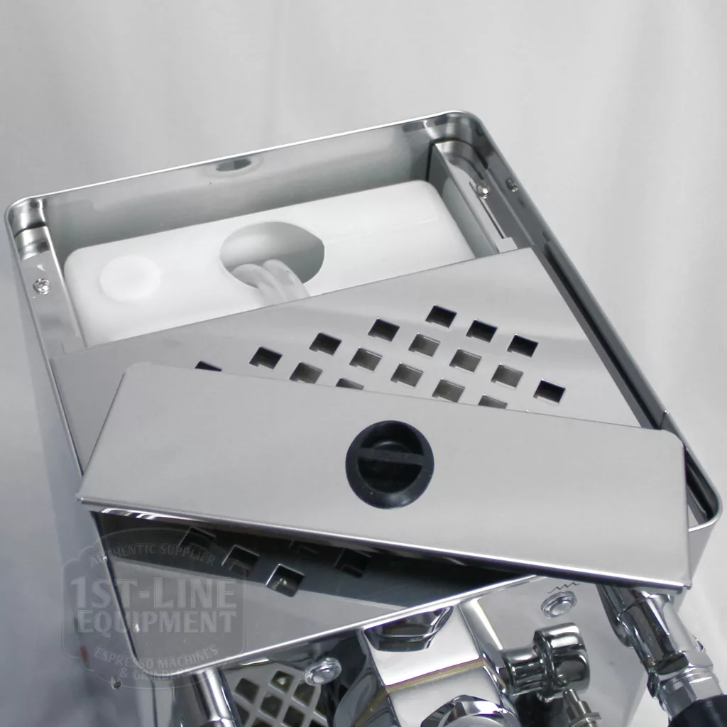 A close-up of a stainless steel espresso machine with the top cover partially removed, revealing a white water reservoir inside. The machine is shiny and reflective, with a modern design. © 2025 1st-line.com