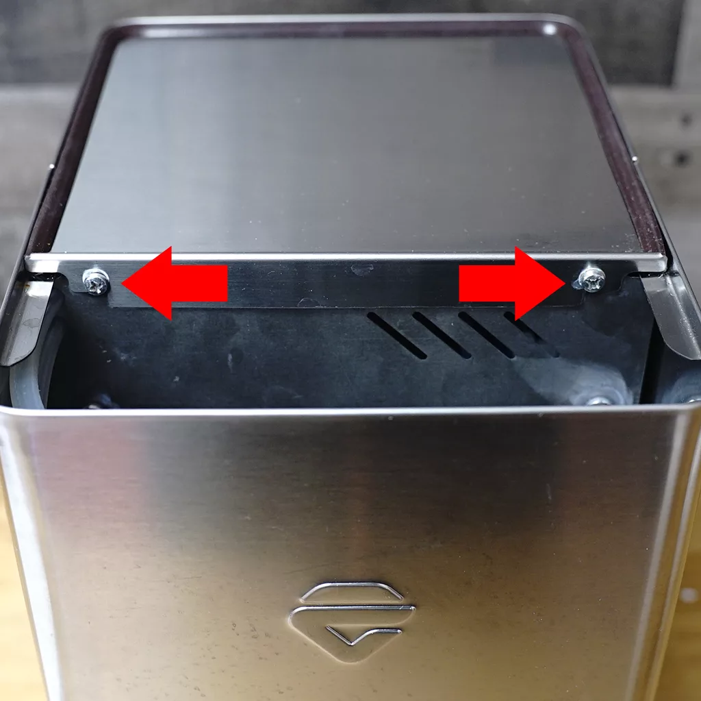 A close-up of a metal container with two red arrows pointing to screws on its top edge, indicating parts that may need to be unscrewed or removed. &copy; 2025 1st-line.com