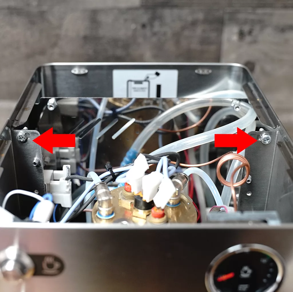 The inside of a coffee machine with exposed wires, tubes, and components; two large red arrows point to screws in the metal frame on either side. &copy; 2025 1st-line.com