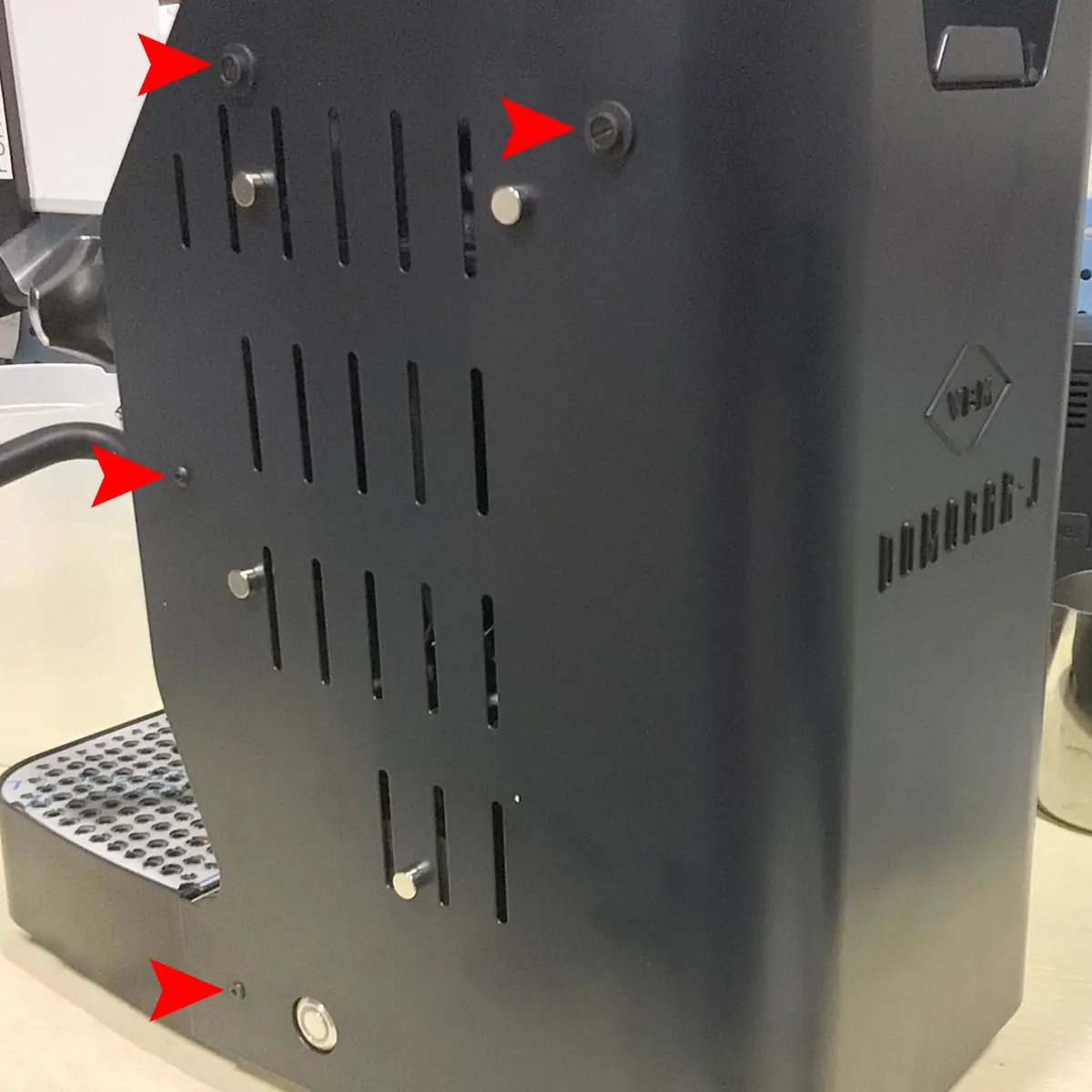 A black coffee machine is shown from the side; red arrows point to several screws and fasteners on the machine’s side panel. © 2025 1st-line.com