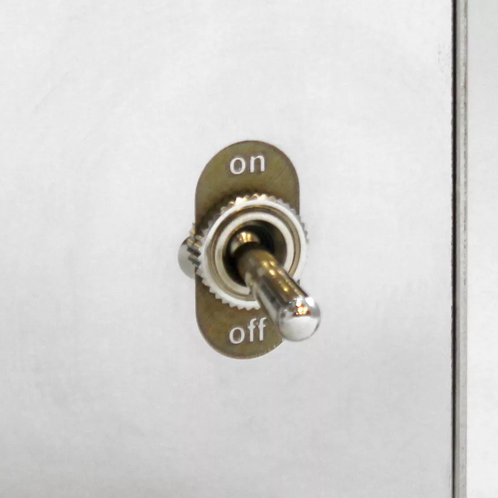 A close-up of a metallic toggle switch mounted on a gray panel, with on labeled above and off below the switch. The switch is currently set to the on position. © 2025 1st-line.com