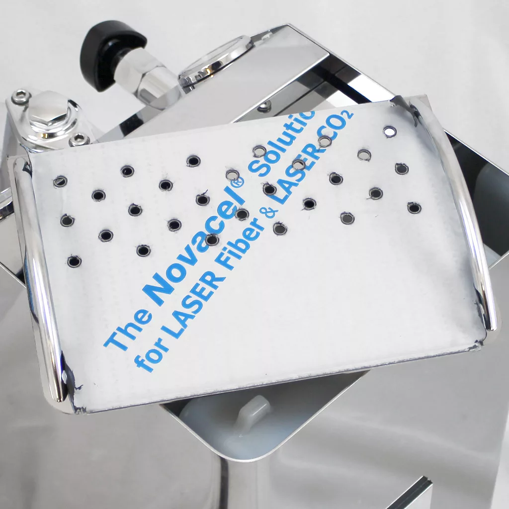 A close-up of a metal medical device with a perforated tray labeled The Novace® Solution for LASER Fiber & LASER CO2 in blue text, attached to a shiny, chrome machine. © 2025 1st-line.com