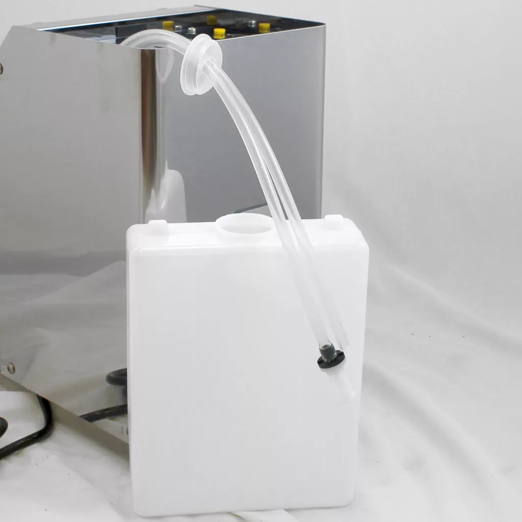 A white plastic water tank with a clear tube attached, positioned next to a metallic machine on a white surface, likely part of a liquid dispensing or filtration system. © 2025 1st-line.com