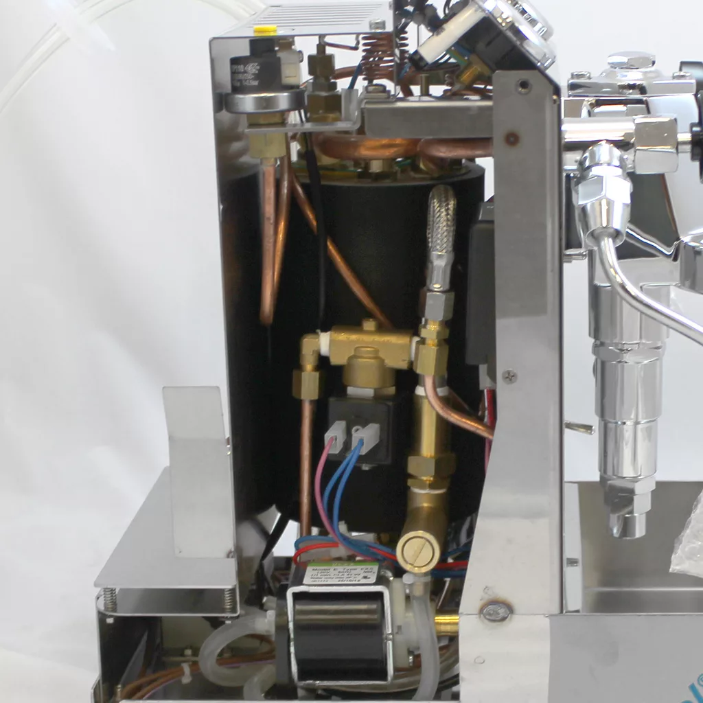 Close-up view of the internal components of an espresso machine, showing copper pipes, wires, connectors, and a pump inside a metal frame, with some parts exposed for maintenance or inspection. © 2025 1st-line.com