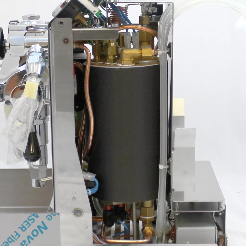 Side view of the internal components of an espresso machine, showing metal pipes, a large cylindrical boiler, copper tubing, and various fittings and cables arranged inside a metal frame. © 2025 1st-line.com