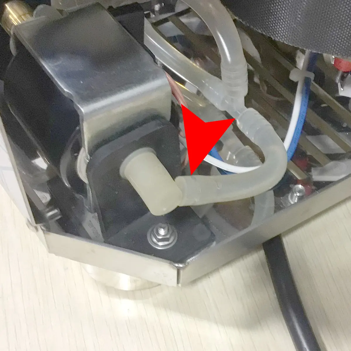 Close-up of a machine’s internal parts with a transparent tube attached to a black component; a red arrow points to the connection between the tube and the component. © 2025 1st-line.com