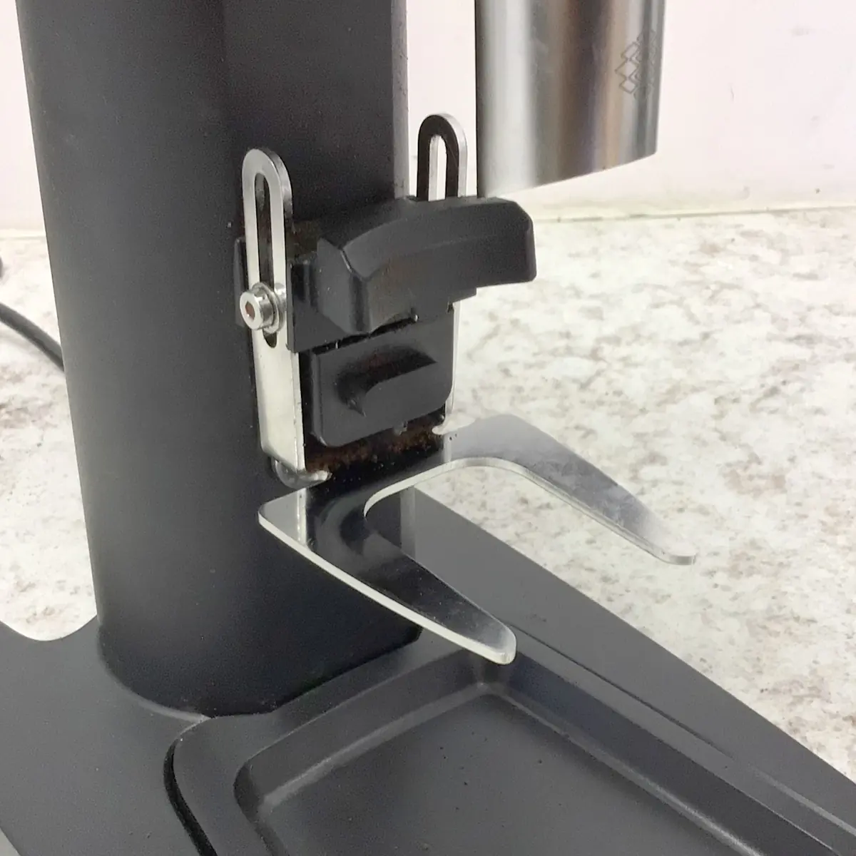 Close-up of the SIDEWALK SALE Pinecone Pinion All-Purpose Espresso Coffee Grinder (showroom demo) metal stand with adjustable clamp and two prongs on a textured countertop—ideal for showcasing at your next Sidewalk Sale. © 2025 1st-line.com