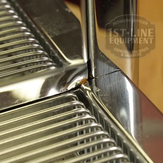 Close-up view of a chrome espresso machine drip tray showing a crack at the corner, with some rust visible along the crack line. © 2025 1st-line.com