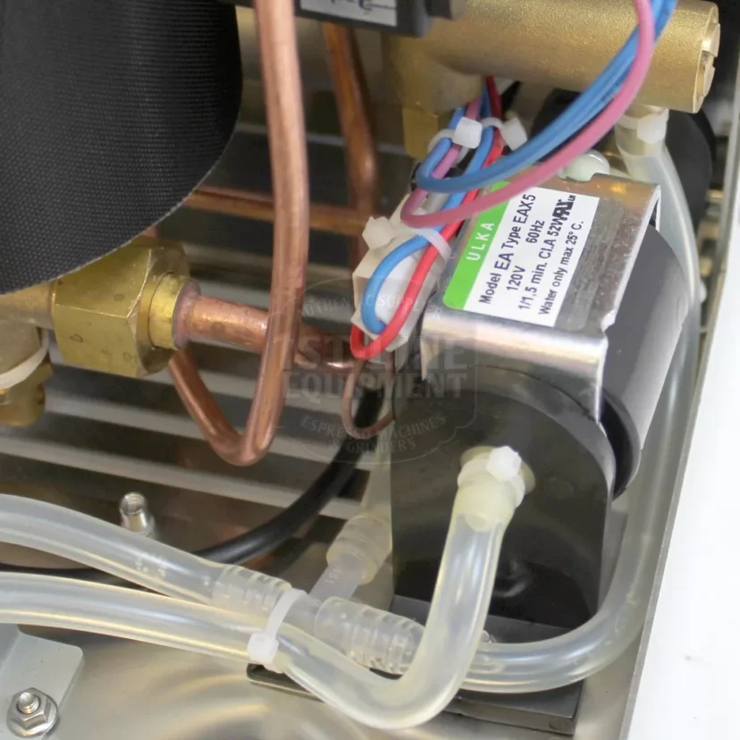 Close-up of internal components of a machine, showing copper pipes, plastic tubing, electrical wires, and a solenoid valve labeled Model EAU-7B1-6AJS with technical specifications. © 2025 1st-line.com