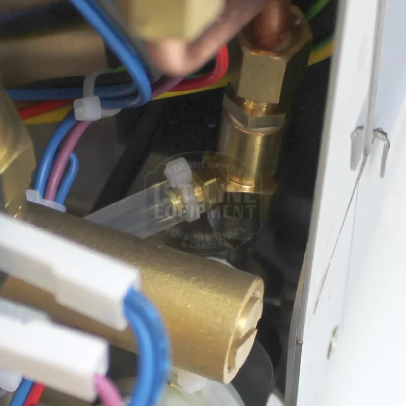 Close-up view of internal components of a machine, showing brass fittings, copper tubing, and various colored electrical wires connected inside a metal enclosure. © 2025 1st-line.com