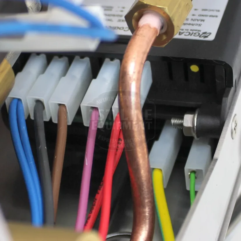 Close-up of electrical wires in various colors connected to white terminal blocks, next to a copper pipe and a black electronic component inside a metallic enclosure. © 2025 1st-line.com