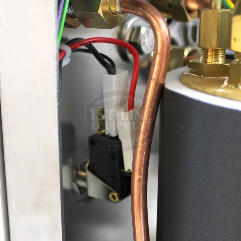 Close-up view of internal components of a machine, showing copper tubing, electrical wires, a black switch, and metal parts, with a partially visible 1st-line Equipment logo in the background. © 2025 1st-line.com