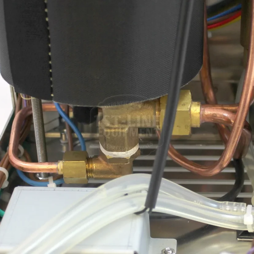 Close-up view of copper and brass plumbing connections inside a machine, with various pipes, wires, and plastic tubing visible in the background. © 2025 1st-line.com
