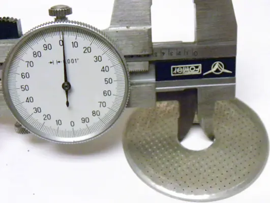 A dial caliper measures the diameter of a perforated metal disc, commonly used as a dispersion screen for espresso machines like the Lelit PL41 Anna. The caliper’s display shows a precise measurement, perfect for your next upgrade. 2025 1st-line.com