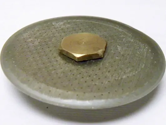 A close-up of a perforated metal shower drain cover with a hexagonal brass nut placed on top, resembling an upgrade or dispersion screen for the Lelit PL41 Anna, set against a plain white background. 2025 1st-line.com