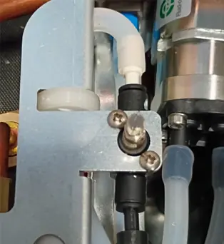 Close-up of a mechanical assembly with metal parts, screws, white and black plastic connectors, and clear tubing—possibly showing Elektra EVOK Internal Valve Adjustments within a machine’s internal mechanism. 2025 1st-line.com