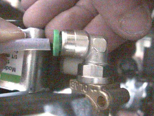 A close-up of a person's hand attaching a clear tube with a green fitting to a metal solenoid valve, possibly as part of plumbing or mechanical assembly. 2025 1st-line.com