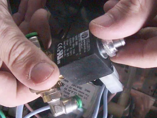 Close-up of hands performing solenoid valve repair, installing or adjusting a small black electrical component with wires and connectors, possibly part of a Lelit Anna or Lelit PL41 espresso machine. 2025 1st-line.com