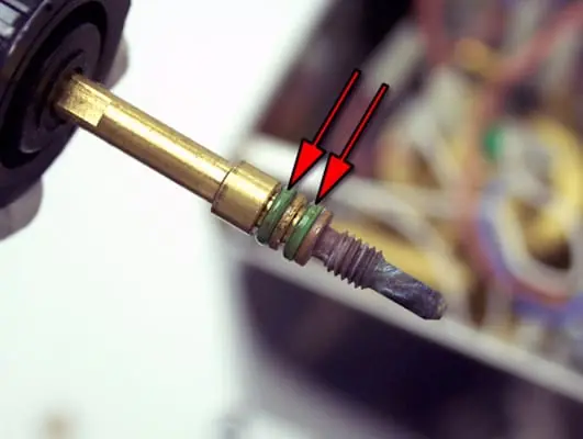 Close-up of a brass rod with two green O-rings highlighted by red arrows, part of a Steam valve repair for the Lelit PL41 Anna espresso machine—note the threaded metal tip and blurred machinery in the background. 2025 1st-line.com