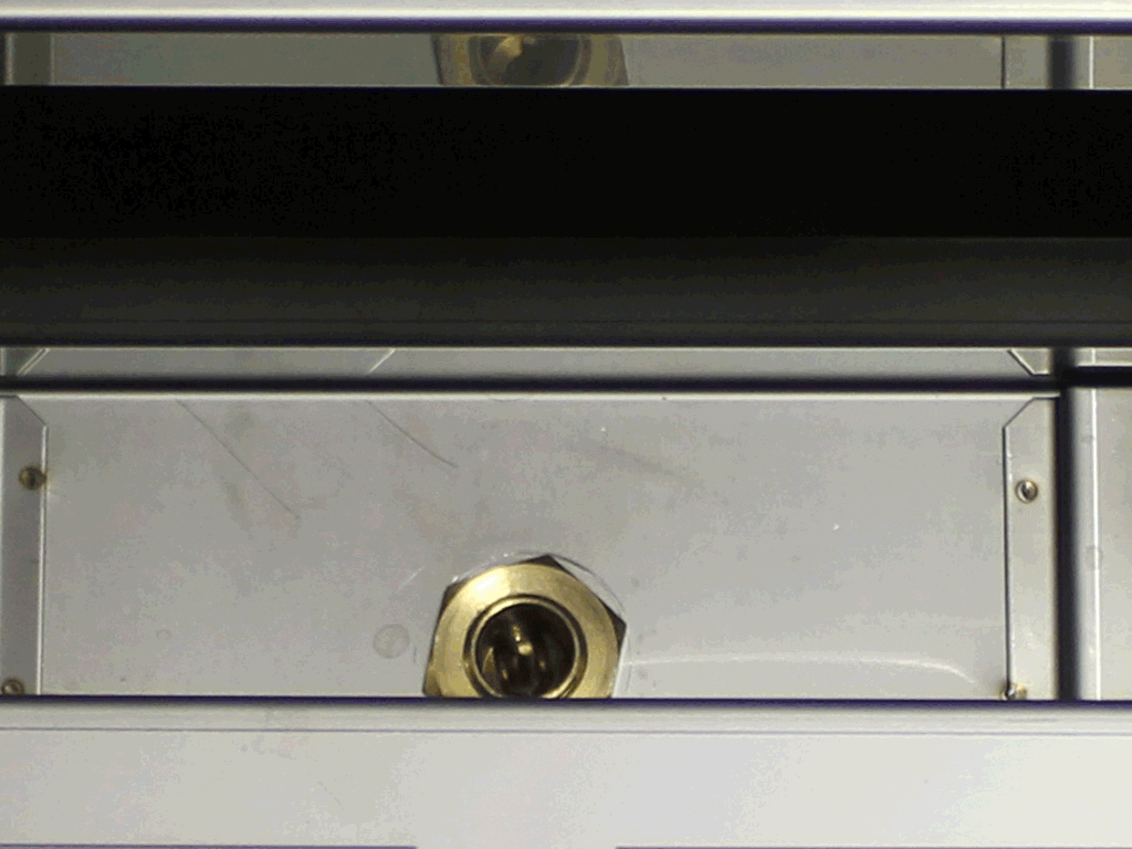 Close-up of a metallic surface featuring a central hexagonal brass fitting, often seen in Direct Connect Conversion setups, surrounded by reflective metal panels and bordered by horizontal black and silver bars. 2025 1st-line.com