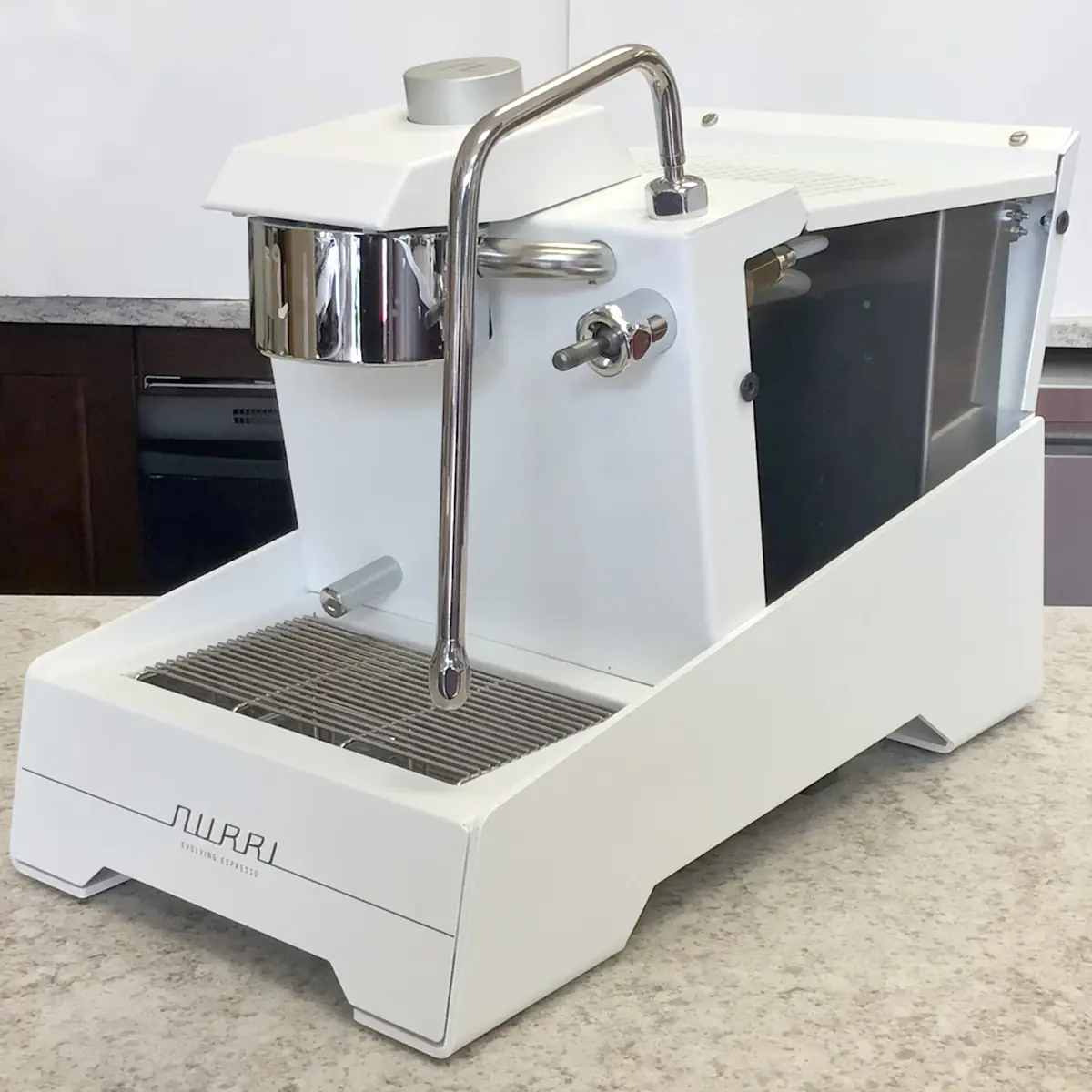 A refurbished white SIDEWALK SALE Nurri R-TYPE SB (HX) Espresso Machine with chrome steam wand and portafilter sits on a speckled countertop in a kitchen. 2025 1st-line.com
