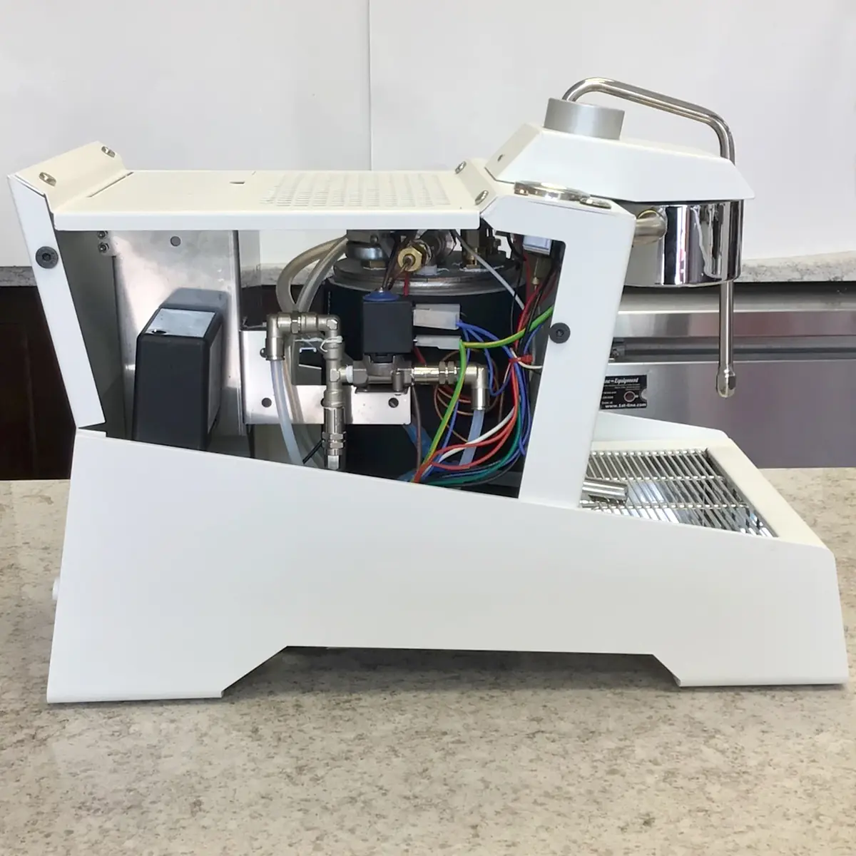 A SIDEWALK SALE Nurri R-TYPE SB (HX) Espresso Machine (RETURNED & REFURBISHED), shown with its side panel removed to display internal components and colorful wiring, sits on a light gray kitchen countertop. 2025 1st-line.com