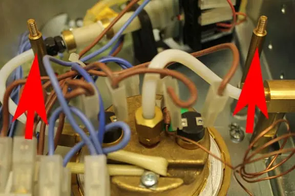 Close-up of a mechanical device with copper wires, white tubing, and connectors; two large red arrows point to specific white tubes inside the assembly, illustrating how removing top cover unveils the intricate inner workings. 2025 1st-line.com