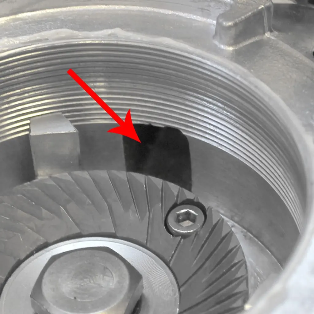 A close-up of Quamar Q50 grinder burrs inside a coffee grinder, with a red arrow pointing to a chipped section on the burr’s edge, highlighting potential issues when accessing the inner components.