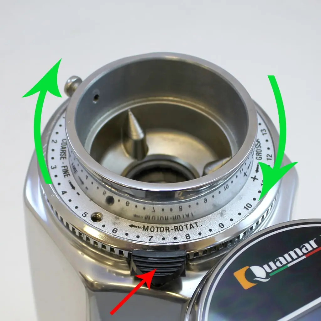 Close-up of a Quamar Q50 coffee grinder’s adjustment ring, with green arrows for fine and coarse settings. A red arrow points to the lever set at 7, illustrating burrs adjustment for precise grinding.