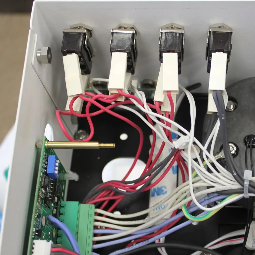 Close-up of an open electronic device showing multiple red and white wires connected to four switches, a circuit board with green terminals, and various internal components.