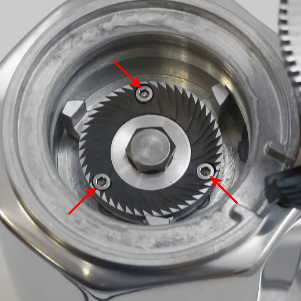 Close-up view of Quamar Q50 burrs, with three red arrows pointing to screws securing the burr inside the metal grinder housing.