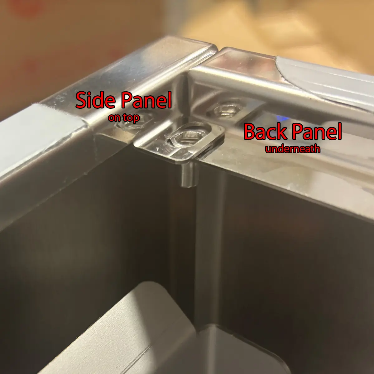 Close-up of metal panels joined at a corner on the Bezzera Sole, labeled &ldquo;Side Panel on top&rdquo; and &ldquo;Back Panel underneath&rdquo; in red text, showing how the panels overlap for accessing the inside during assembly.